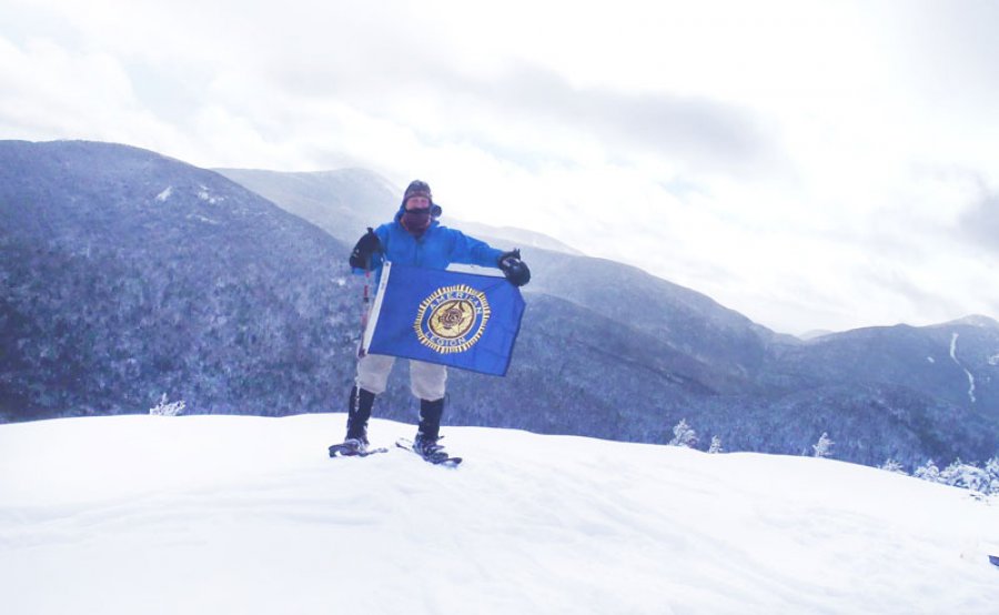 Keith Koster atop one of the 46 high peaks in New York holding the American Legion flag.  Photo provided.